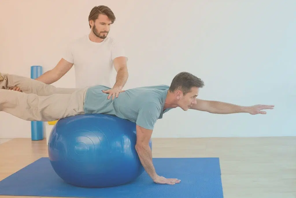 Male physical therapist showing a patient how to balance on a workout ball.