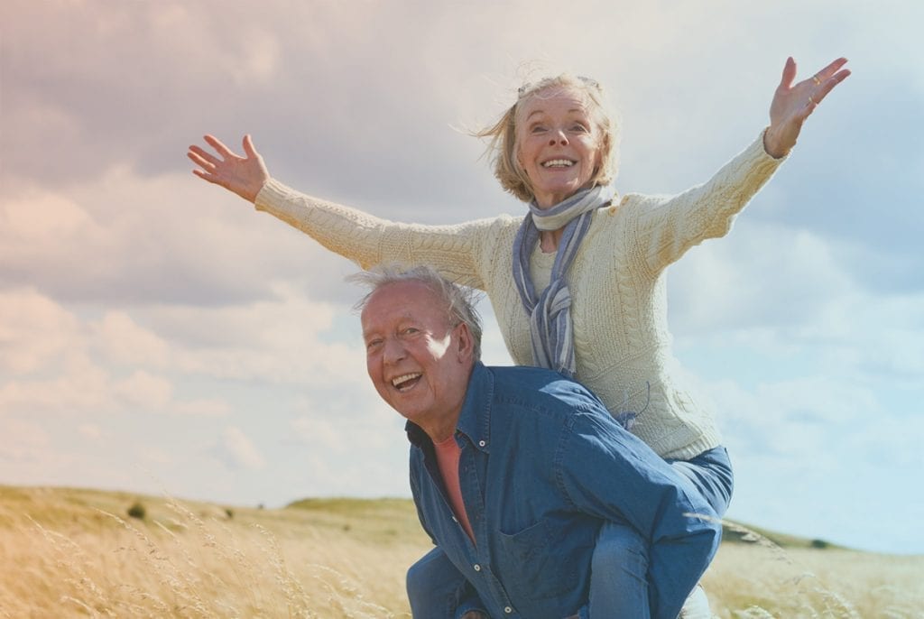 Older couple giving each other a piggy back ride in a open field.