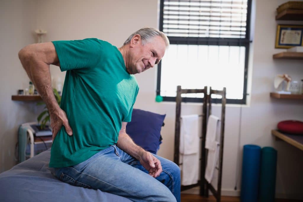 Elderly man holding his lower back due to pain.