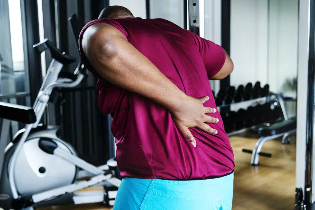 Young man holding his back due to pain in the gym