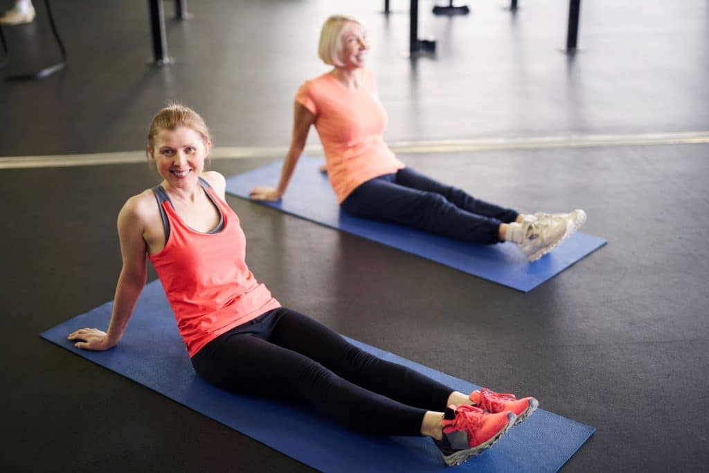 two women on yoga mats doing leg stretches