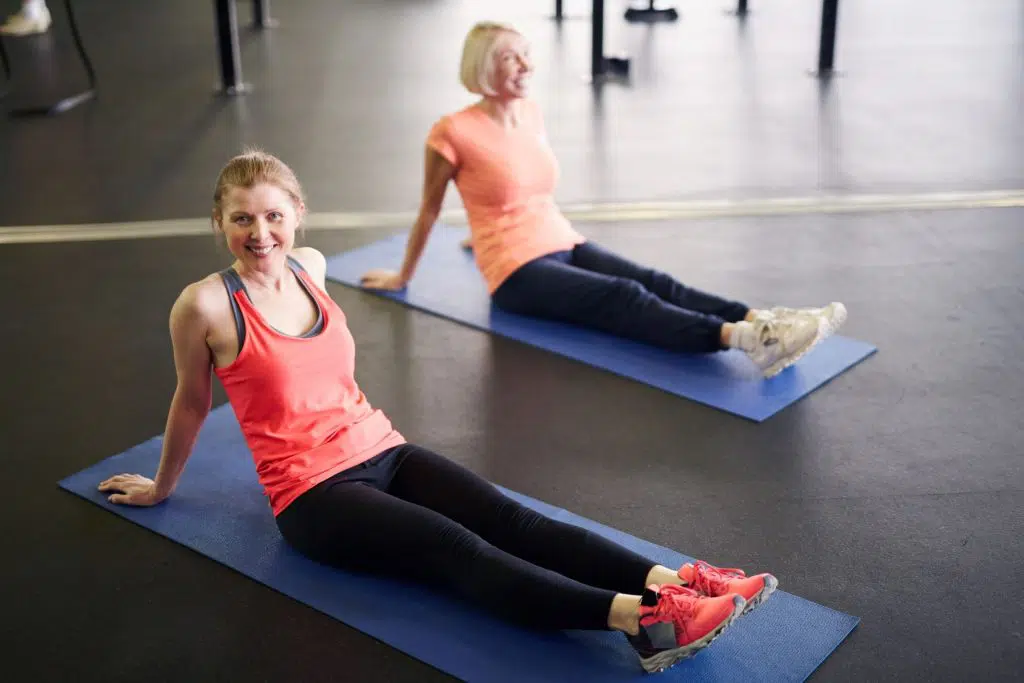 two women on yoga mats doing leg stretches