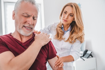 Doctor making medical examination on patient shoulder in clinic while he feeling pain