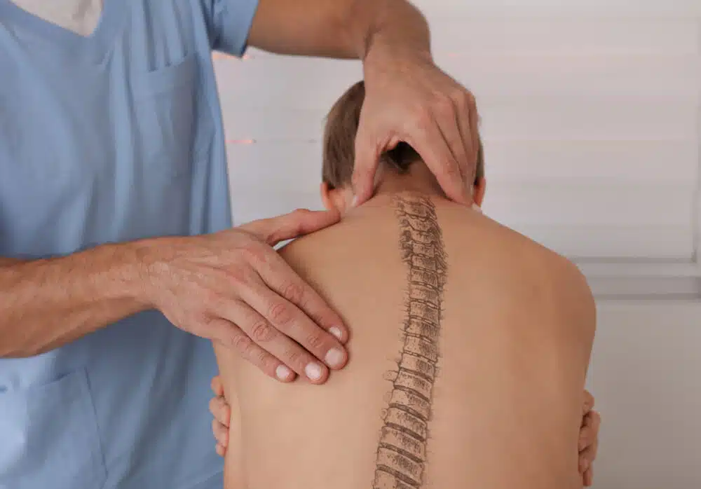 Chiropractor is examining a boy back who suffers from scoliosis.