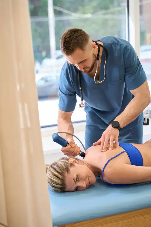 chiropractor applying personalized shockwave therapy treatment in torrance on female patient's upper back 