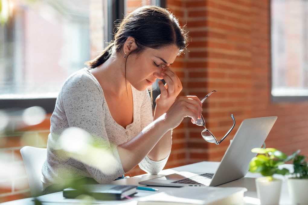 Female holding her head from a headache while in front of her laptop | Headache and Migraine Treatment