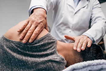 chiropractor in white coat massaging neck of man with muscle weakness